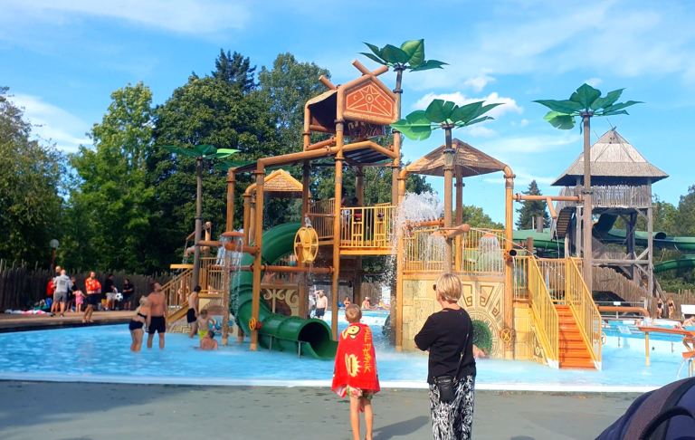 Vattenland med lekplats, träd, palmträd och familjer som leker vid poolen.