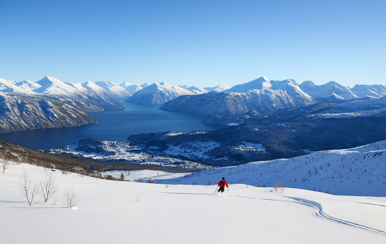 Illustration av Snötäckta berg och en fjord med en skidåkare i röd jacka i förgrunden.