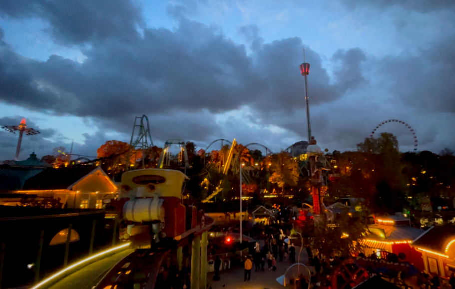 Vackert nöjesfält med åkattraktioner och besökare under en kvällshimmel. Lamporna lyser i höstmörkret på Liseberg 