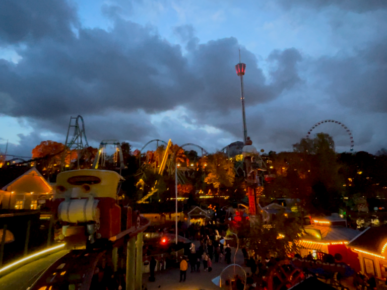 Nöjespark med attraktioner under en molnig himmel, människor i rörelse.