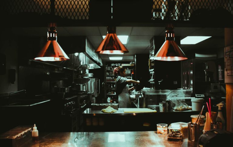 Köksmiljö med dämpad belysning och kock som arbetar bakom en disk.