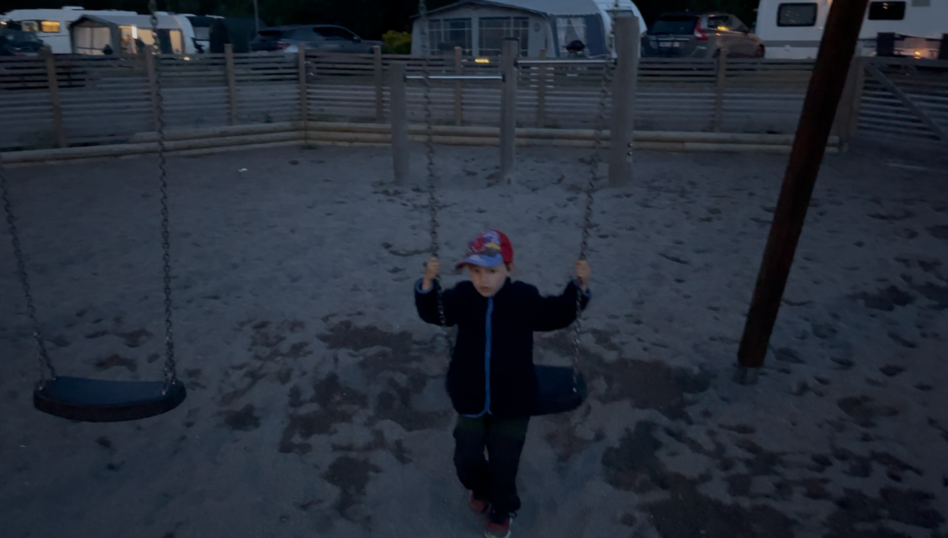 Gungan på Lekplatsen Ett barn i röd mössa leker på gungor på en sandig lekplats.