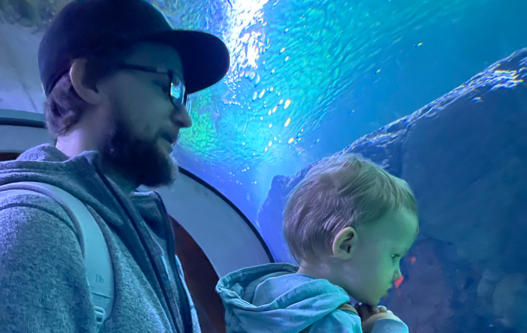Man och barn tittar på akvariefiskar bakom ett glasfönster.