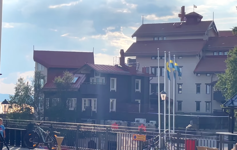 Vy över byggnader med röd tak och svenska flaggor vid en hamn.