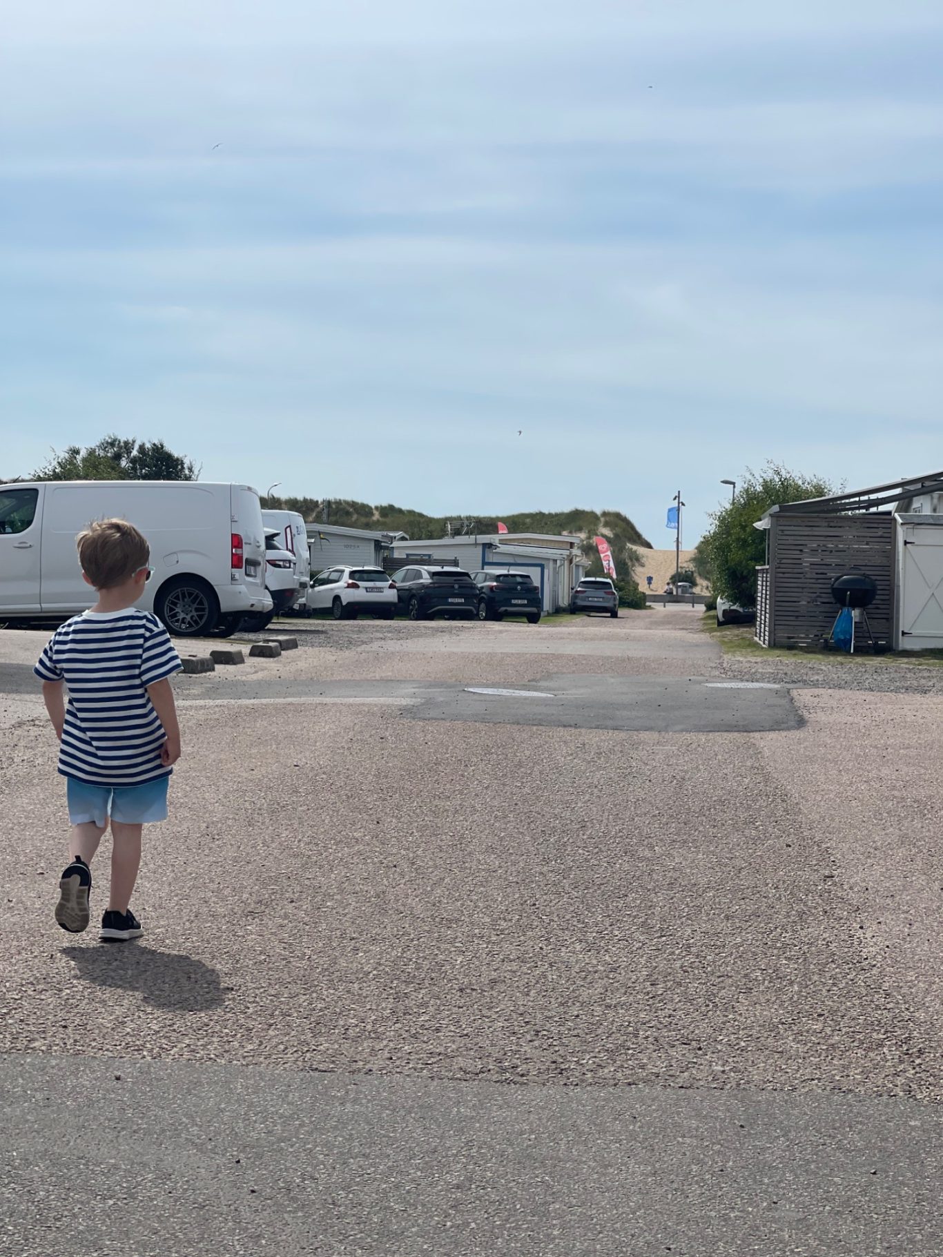 Mot Skrea Strand Ett barn går längs en väg bland husvagnar och parkerade fordon.