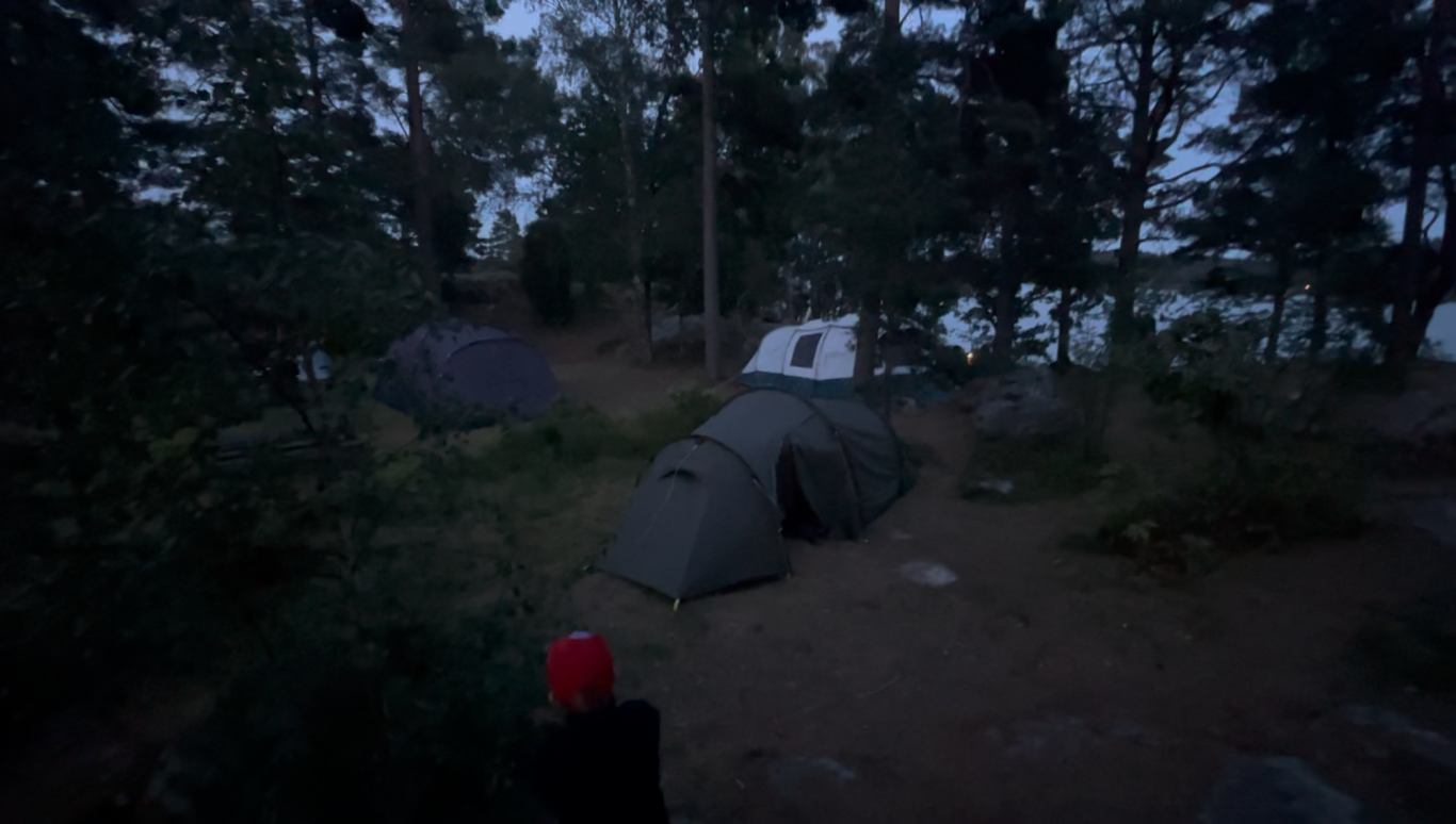 Vår Tältplats Tält på en campingplats i skymning med skog och vatten i bakgrunden.