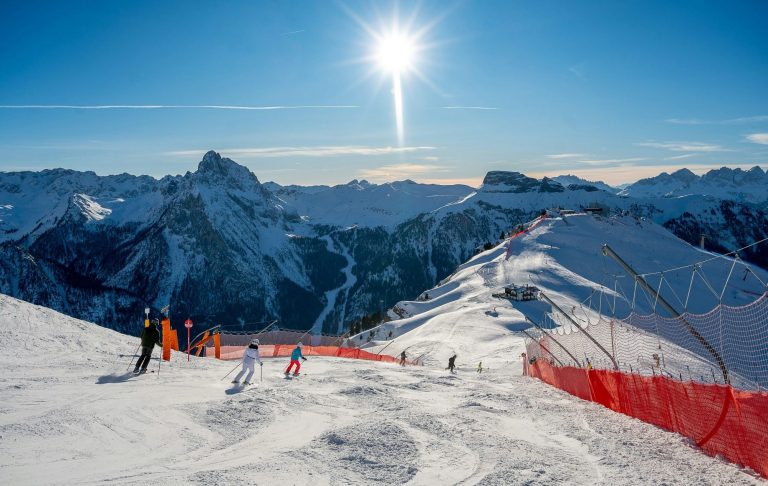Pistskidåkare på en snötäckt bergstopp med solen som skiner ovanför.