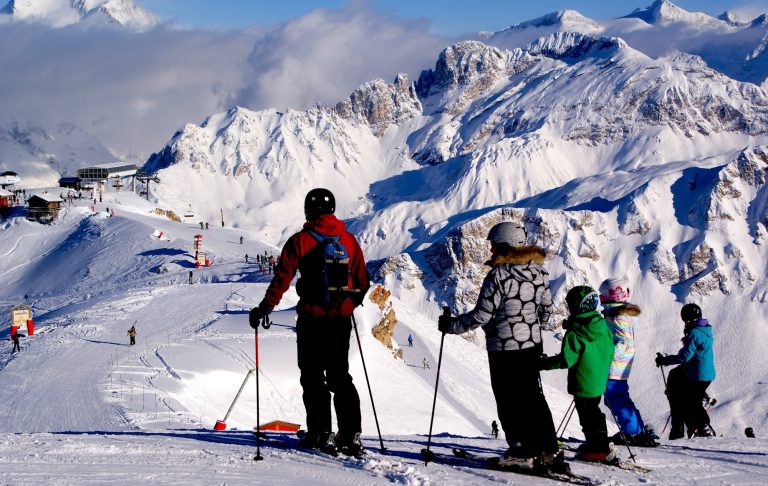 Skidåkare på en bergstopp med snötäckta alpberg i bakgrunden.