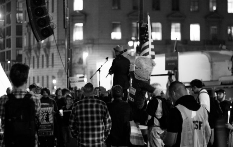 Folkmassan samlas vid en scen, en talare med flagga i bakgrunden.