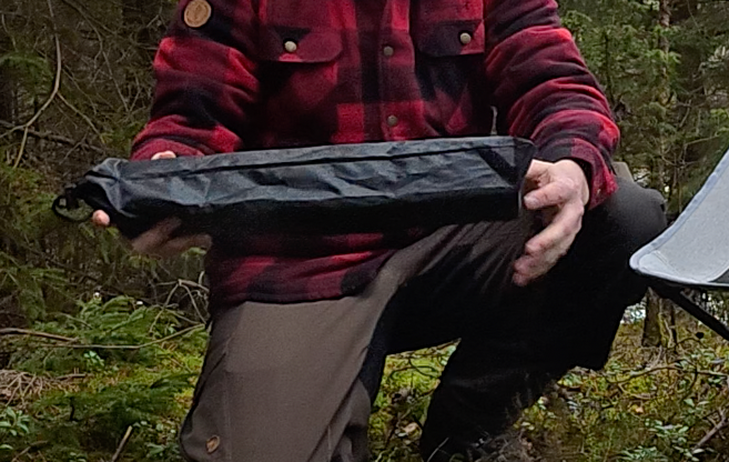 Person i röd och svart rutig jacka håller i ett ihopfällbart campingbord.