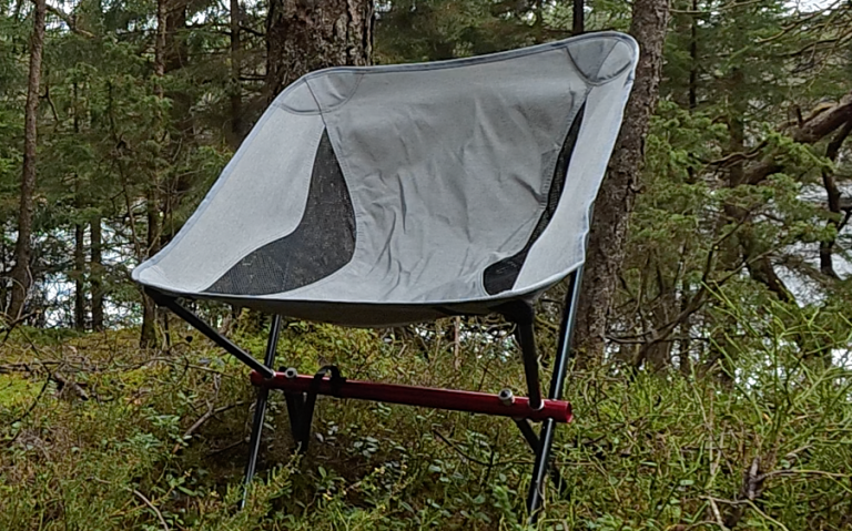 En hopfällbar, grå ultralätt campingstol i en skogsmiljö.