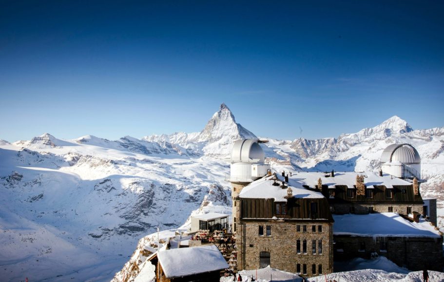 Snötäckt bergskedja med Matterhorn i bakgrunden och en byggnad i förgrunden.