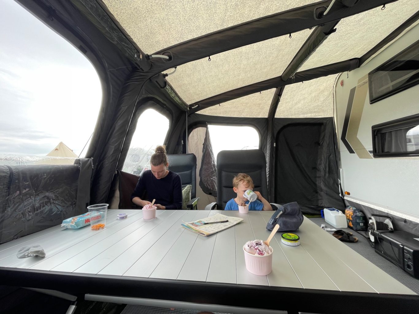 Glass I förtältet Två personer sitter vid ett bord i en campingbil, med teckningsmaterial framför sig.