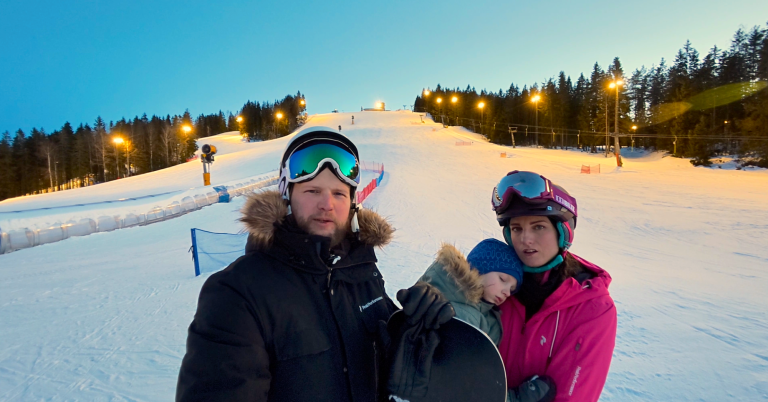 Familj på skidort vid solnedgång, omgiven av snö och skidbackar.