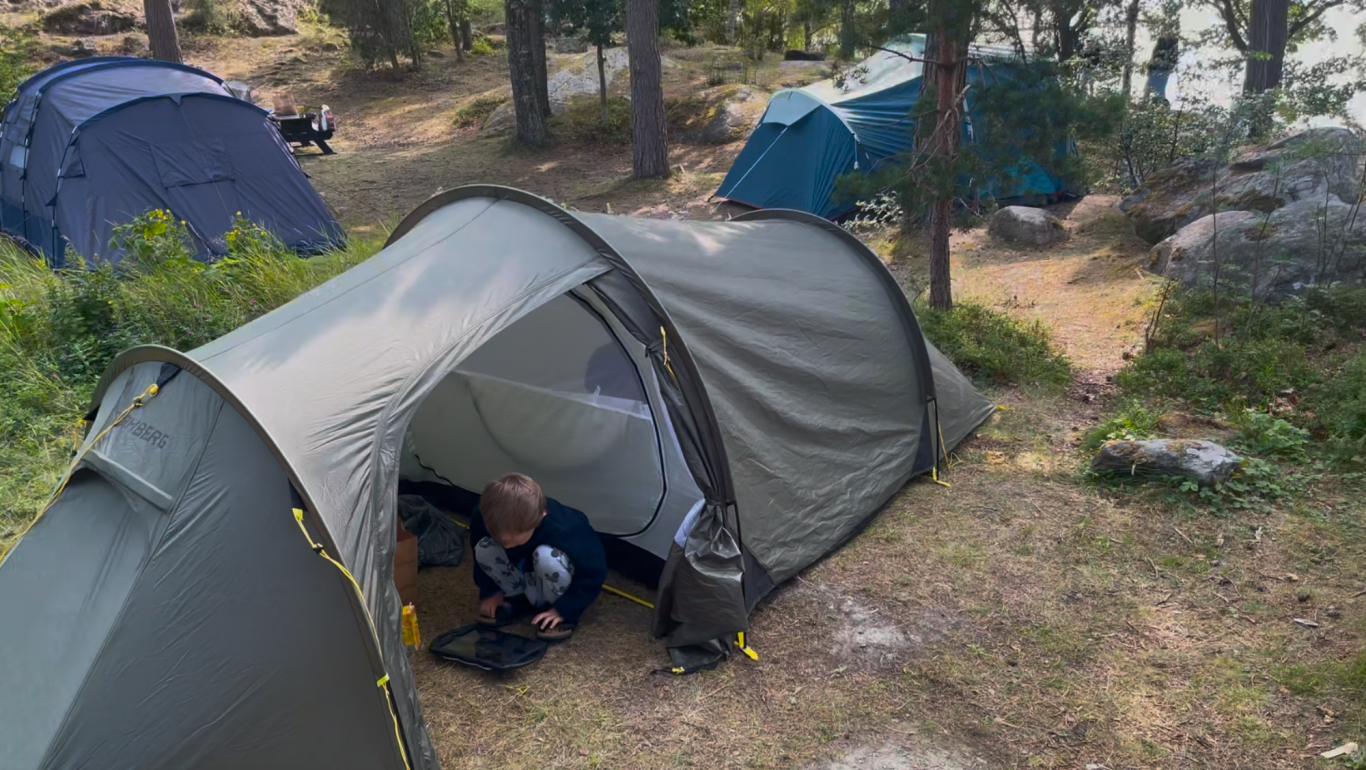 Vårt tält Tält i skog med en liten pojke som leker inne i tältet.