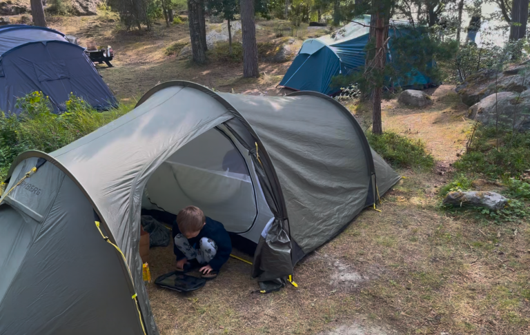 Tält med ett barn som leker, omgiven av träd och andra tält.