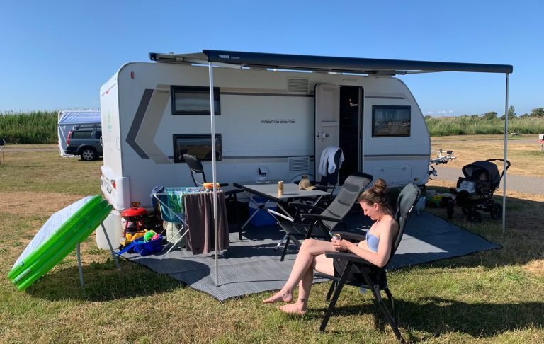 En person sitter på en stol utanför en husvagn på en campingplats leksaker runt vagnen.