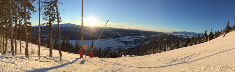 Panoramabild av snöklädda fjäll och solnedgång över dalen.