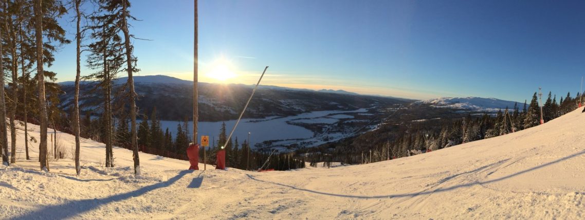 Panoramabild av snöklädda fjäll och solnedgång över dalen.