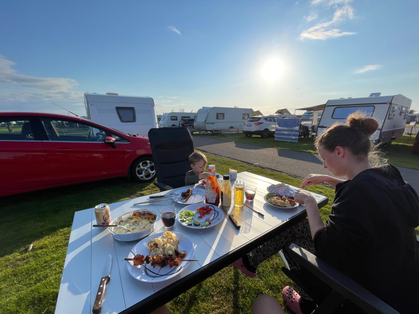 Middag i solen Två personer äter middag utomhus vid en campingplats i soligt väder.