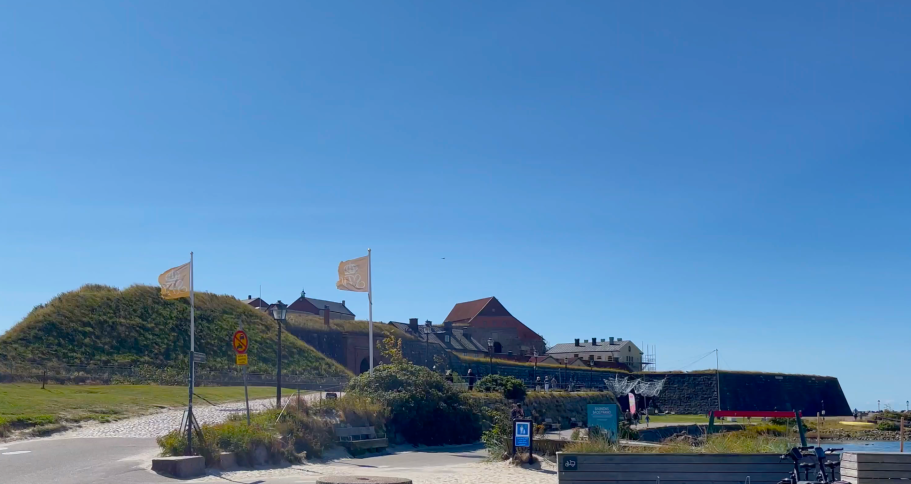 Utsikt över en kulle med byggnader och flaggor i ett klart blått himmel.