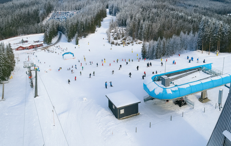 Skidbacke med människor, lifta och snötäckta träd i bakgrunden.