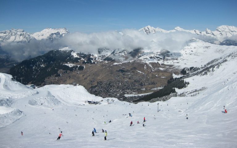 Skidåkare på snötäckta backar med fjäll och dalar i bakgrunden.