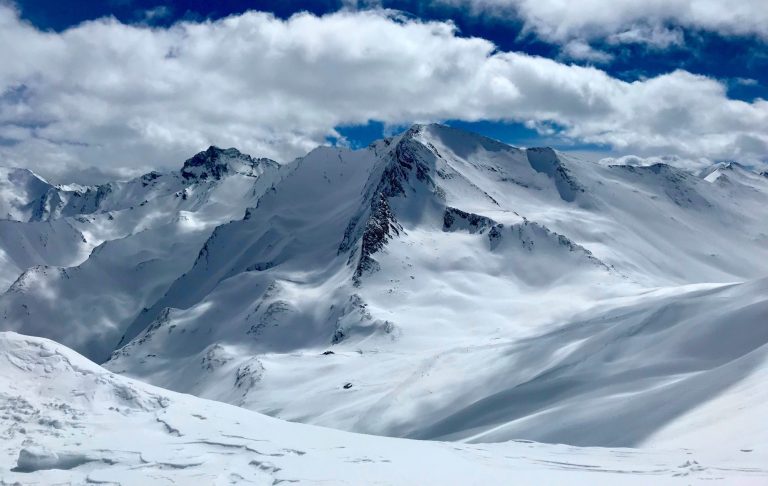 Snötäckta bergstoppar och molnig blå himmel i fjällmiljö.