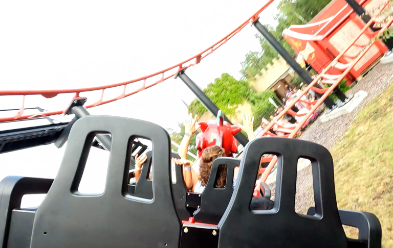 En berg- och dalbana med röda vagnar och gröna omgivningar.