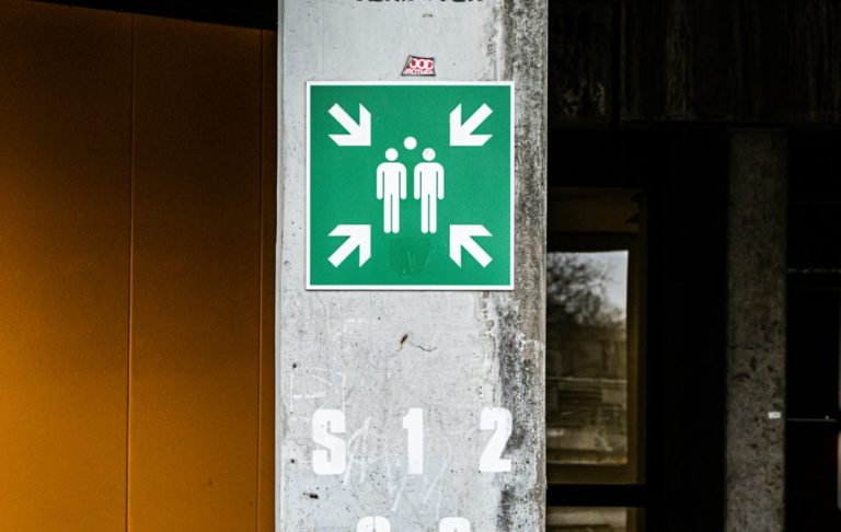 Nödsituation skylt med pilar som pekar mot utrymningsvägar och två figurer.