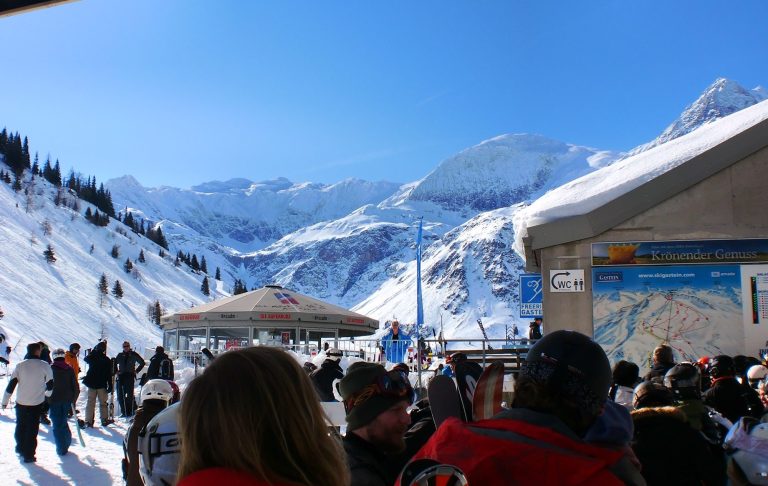 Människor på en skidort med snötäckta berg och klarblå himmel.
