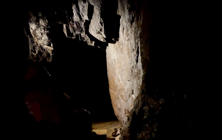 Mörk gruva med stenar och en svag ljuskälla som framhäver formen av bergväggen.