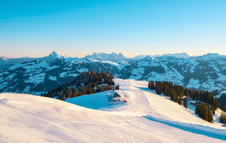 Vinterlandskap med snöklädda alpberg och ett litet hus på en kulle.
