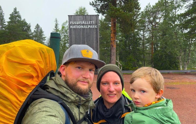 En familj med ryggsäckar i naturen; en vuxen och ett barn står tillsammans.