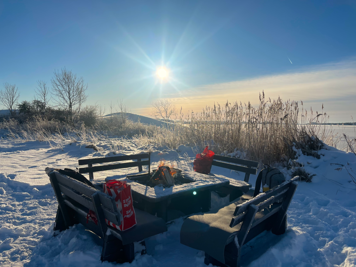 Grillplats Tjolöholms Slott Ett vinterlandskap med en sittgrupp omgiven av snö och solnedgång i bakgrunden.