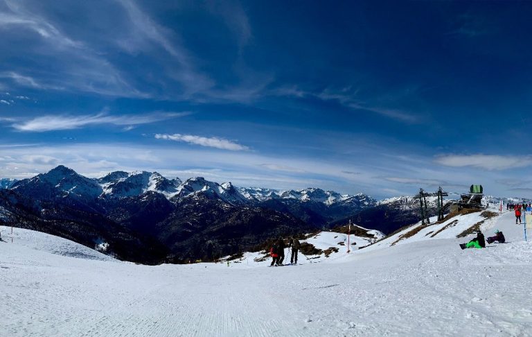 Sestriere - Italien Vinterlandskap med snötäckta alpberg och klarblå himmel, skidåkare i bakgrunden.