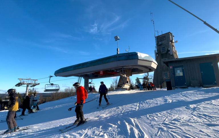 Skidåkare vid en stollift på en solig, snöig dag i fjällen.
