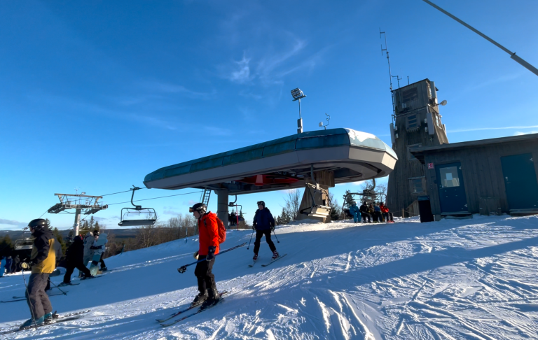 Skridskårare vid en skidlift på snötäckta backar under en klar, solig dag.