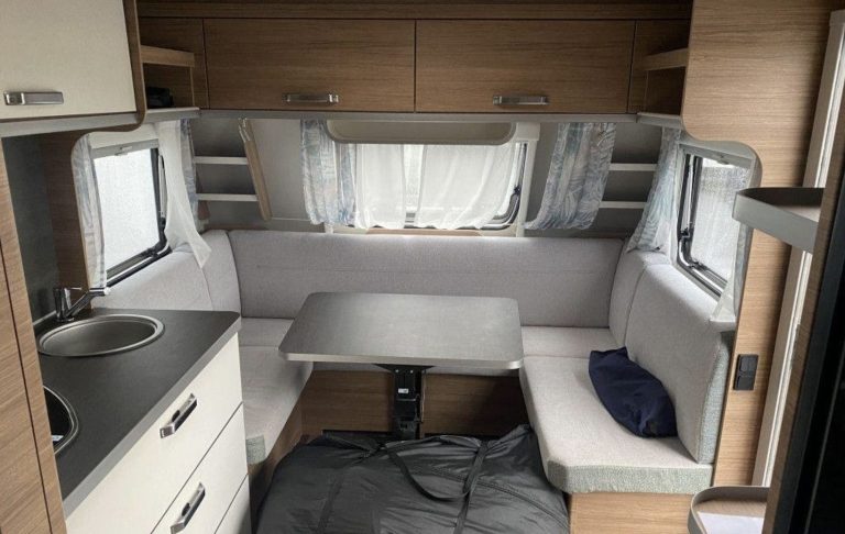 Weinsberg CaraOne 550Uk soffdelen Inre i en husvagn med kök, sittgrupp och fönster, ljusa trämaterial och neutral färgsättning.