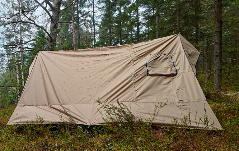 Ljusbrun tält i skog med träd i bakgrunden.
