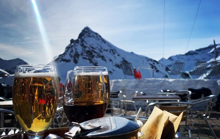 Två ölglas med snöklädda alpberg i bakgrunden och turistområden.