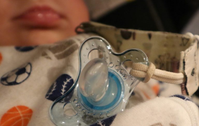 Närbild av ett spädbarn med napp och sjukhusarmband.