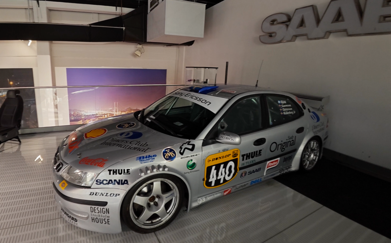 Rallybil Racerbil med silverfärg och racingdekal, stående i en modern utställningslokal.