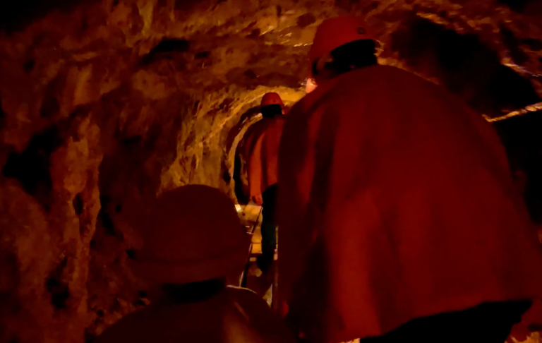 Två personer i röda skyddskläder går genom en mörk tunnel.