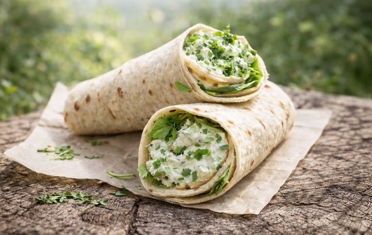 Två tortillawraps med grönsaker på en träskiva i naturmiljö.