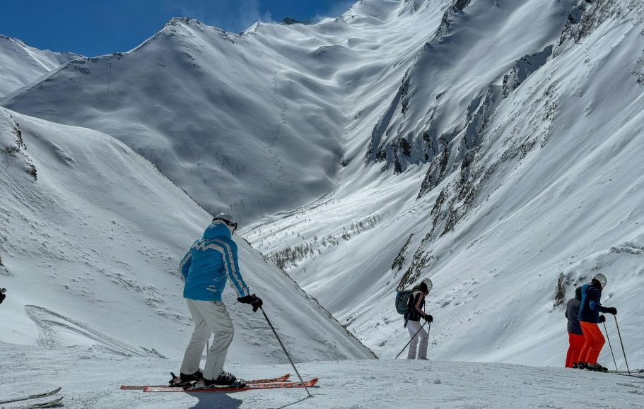 Skridskoåkare på snötäckt berg med majestätiska fjäll i bakgrunden.