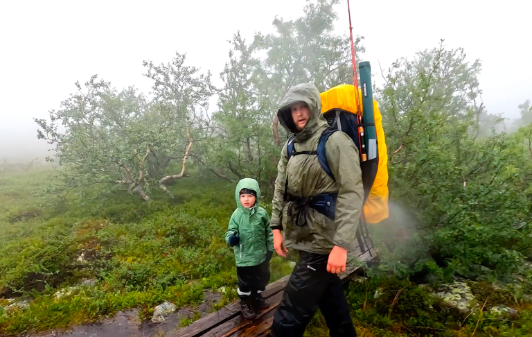 Vandrar i dimma med ett barn i grön jacka, omgiven av ljus vegetation.