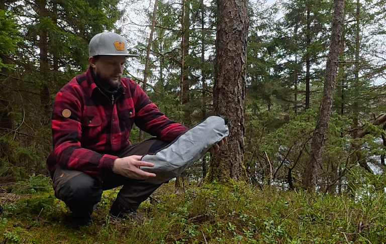 En man knäböjer i skogen och håller en inslagen föremål i handen.
