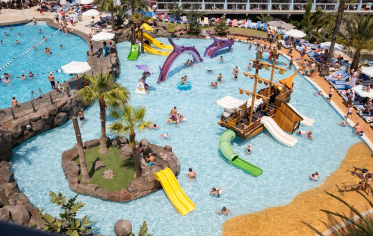 Flera personer leker i en vattenpark med rutschkanor och ett piratskepp.