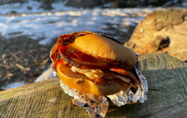 Den perfekta utflyktsmaten en falugkorvsburgare med ägg, inslagen i folie, på en träyta. Snö i bakgrunden.